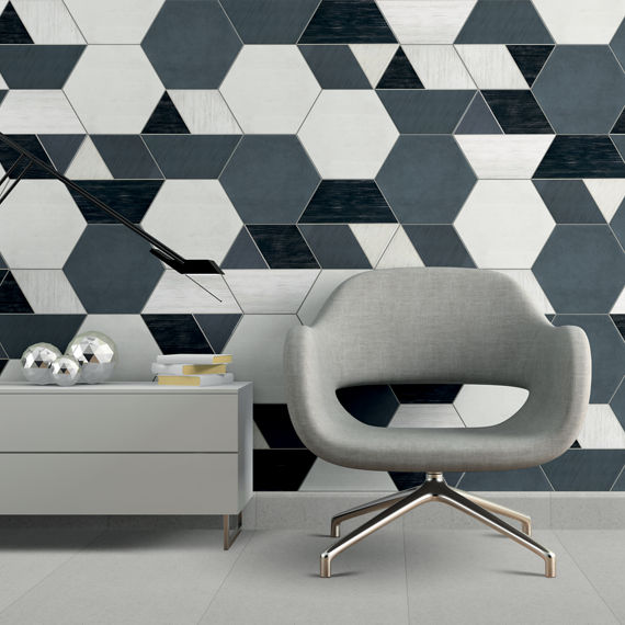 Room with black and white geometric patterned hexagon tile on back wall, white hexagon tile on back wall, and gray hexagon tile on back wall in pattern, gray armchair, and a small gray side table.