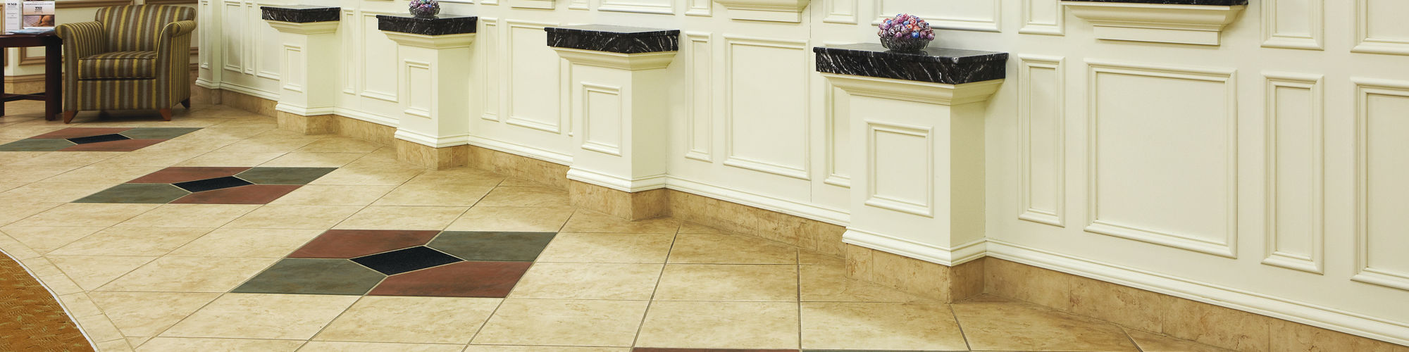Bank with black granite square tile in center of gray and red square tile creating diamond pattern, white counters, greenery on counters, and beige walls.