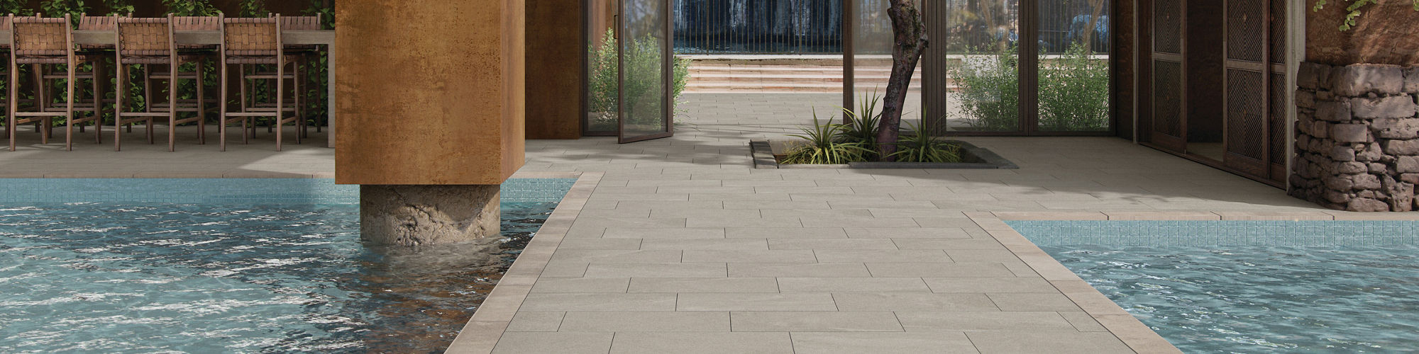 Outdoor pool area with gray stone look rectangle floor tile, two pools, bar area, and greenery.