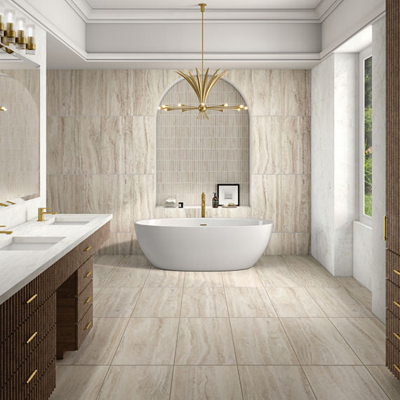 Bathroom with beige stone look rectangle tile on floors and walls, white tub, and gold accents.
