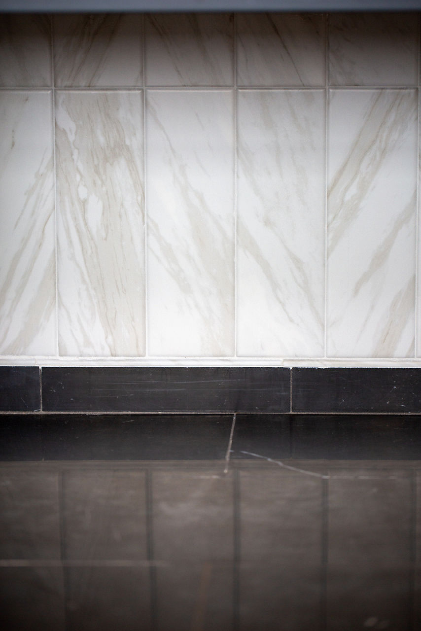 Close up of bathroom floor with black marble look floor tile, white marble look rectangle tile on walls, and black rectangle tile between wall and floor.