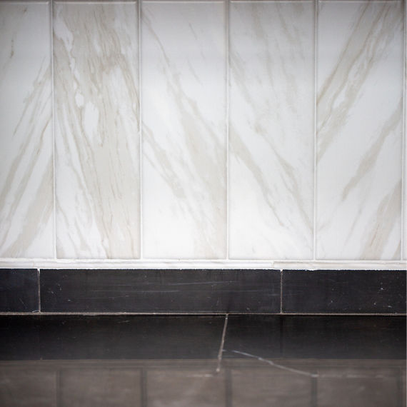 Close up of bathroom floor with black marble look floor tile, white marble look rectangle tile on walls, and black rectangle tile between wall and floor.