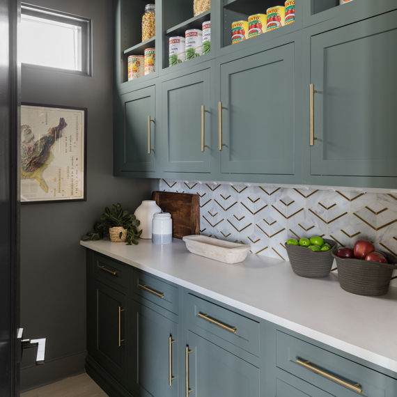 Pantry with white mosaic on backsplash, white concrete look countertop, green cabinets, gray back wall, and gold accents.