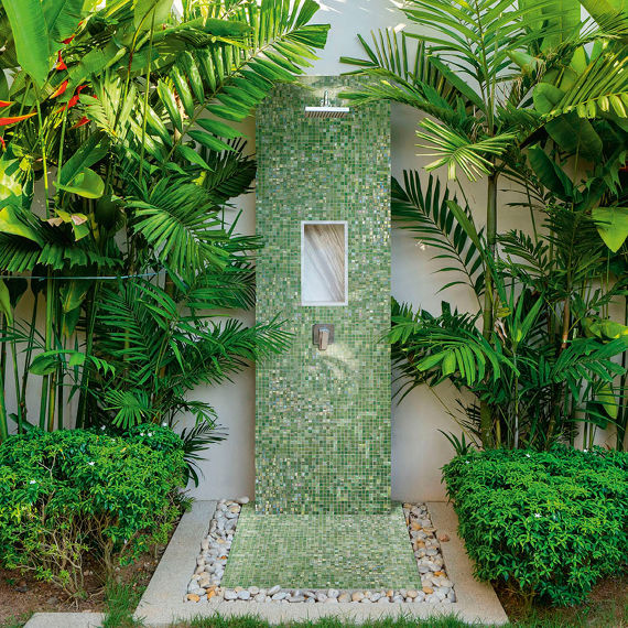 Outdoor shower with green shimmery mosaic tile surrounded by tropical green plants.