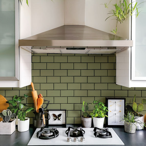 Kitchen with green subway tile on backsplash, gray countertops, white cabinets, and greenery on counter.