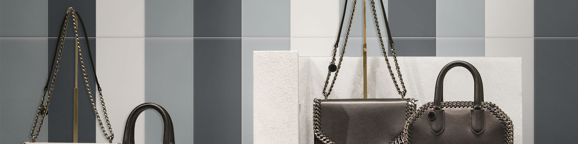 Boutique shop wall with glazed ceramic tile in vertical stripes of grey in different hues. Handbags on a shelf in the foreground.