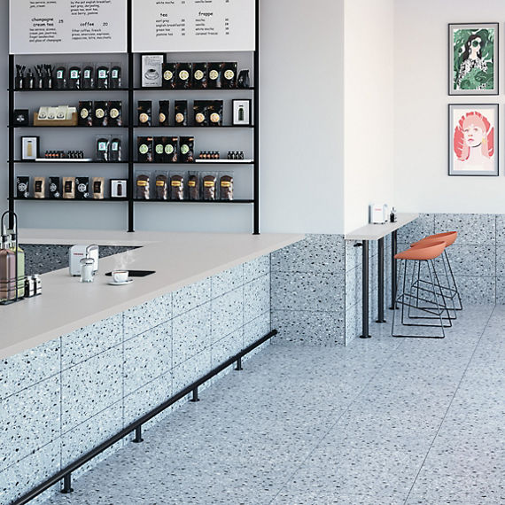 Cafe with white stone look quartz slab on countertop, white walls, orange chairs, and white terrazzo look floor tile.
