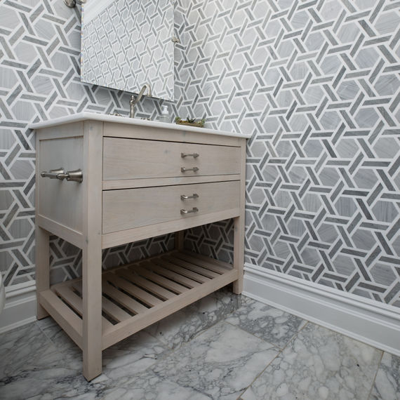 Powder room with gray natural stone rotating hexagon tile on walls, white countertop on sink, and light a brown cabinet.