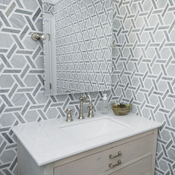 Powder room with gray natural stone rotating hexagon tile on walls, white countertop on sink, and light a brown cabinet.