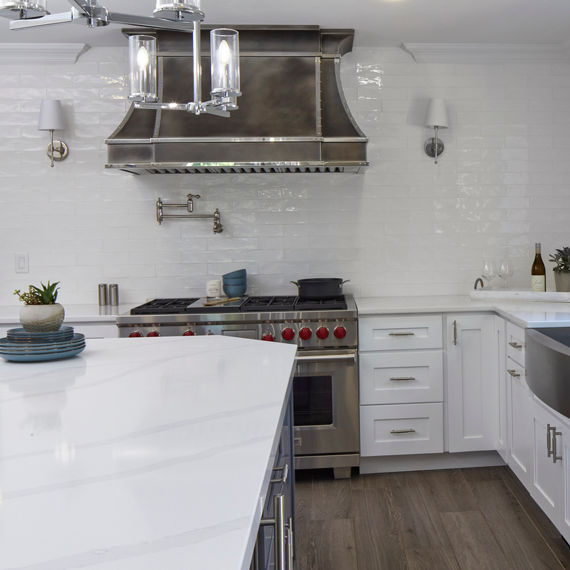 Kitchen with white undulated subway tile on backsplash, white marble look countertop, and white cabinets.