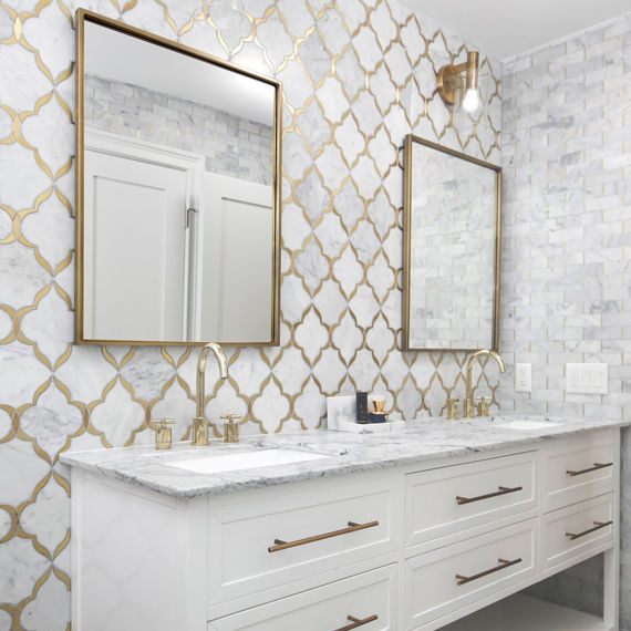 Bathroom with his and hers sinks, and a white marble look mosaic, white countertop, and gold accents.