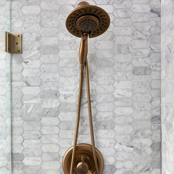 Close up of showerhead and shower with white marble hexagon mosaic on walls.
