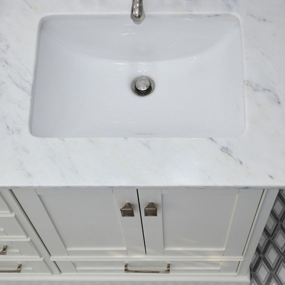 Bathroom overhead view of sink with white countertop and a gray and white harlequin decorative floor.
