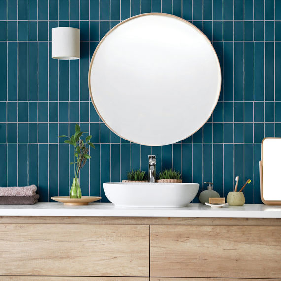 Bathroom with blue rectangle tile on back wall in various sizes, white countertop, wood cabinet, white sink, and round mirror above sink.