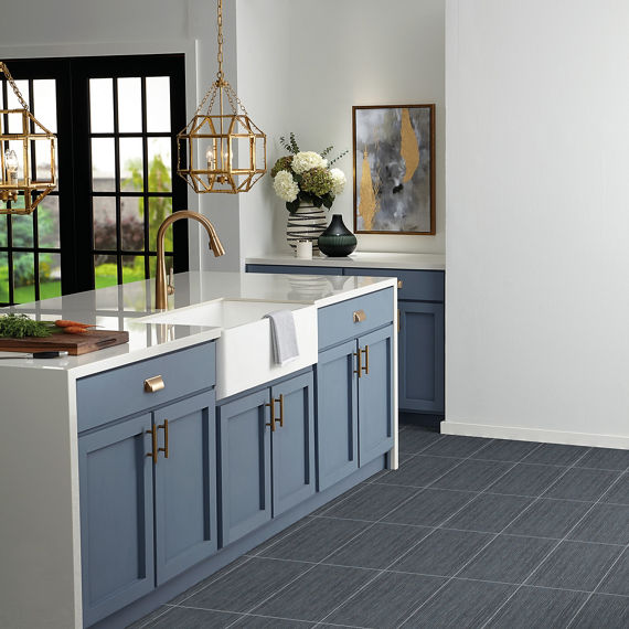 Kitchen with gray rectangle fabric look floor tile, blue cabinets, white countertop, and gold accents.