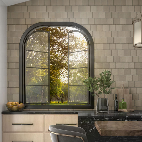 Kitchen window showing greenery outside, light gray square mosaic tile on walls, black countertop, and light wood cabinets.