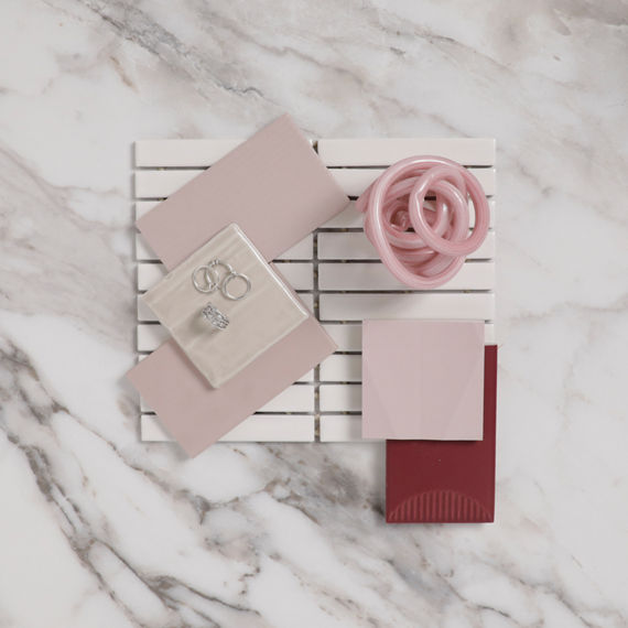 Flatlay with light pink rectangle tile, a large white marble look tile, a dark pink tile with a half moon design, small pink square tile, and silver jewelry on flatlay.