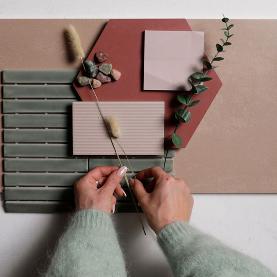 Flatlay with a pink rectangle tile, pink hexagon tile, pink square tile, pink linear tile, green rectangle mosaic tile, and two hands setting down plants on the flatlay.