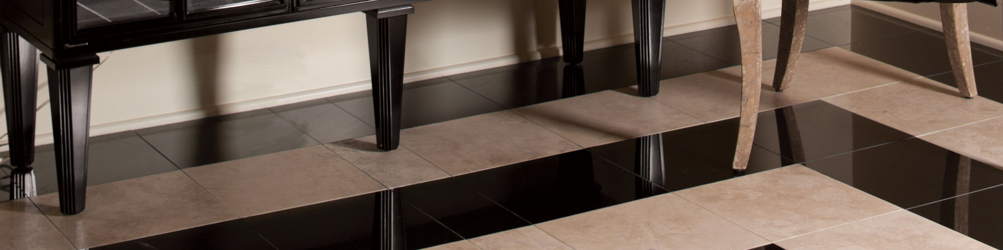 Room with black granite square tile creating a tile rug, beige square tile, and table with mirror doors.