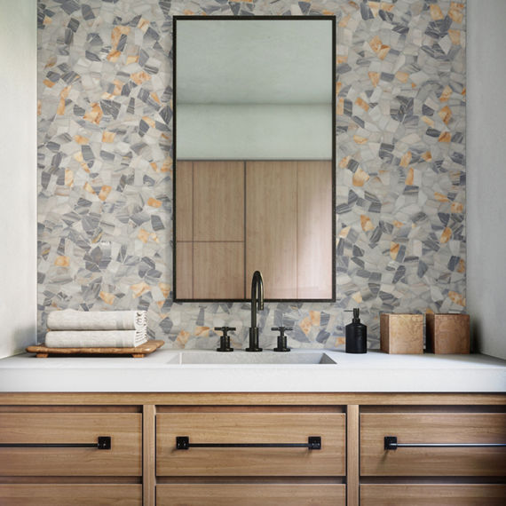 Bathroom with gray pebble mosaic on back wall, wood cabinets, white countertop, black accents, and rectangle mirror above sink.