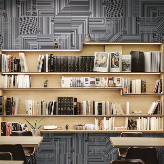 Metallic-look, geometric pattern tile on a library wall.Light wood bookshelves with books and arm chair in the foreground.