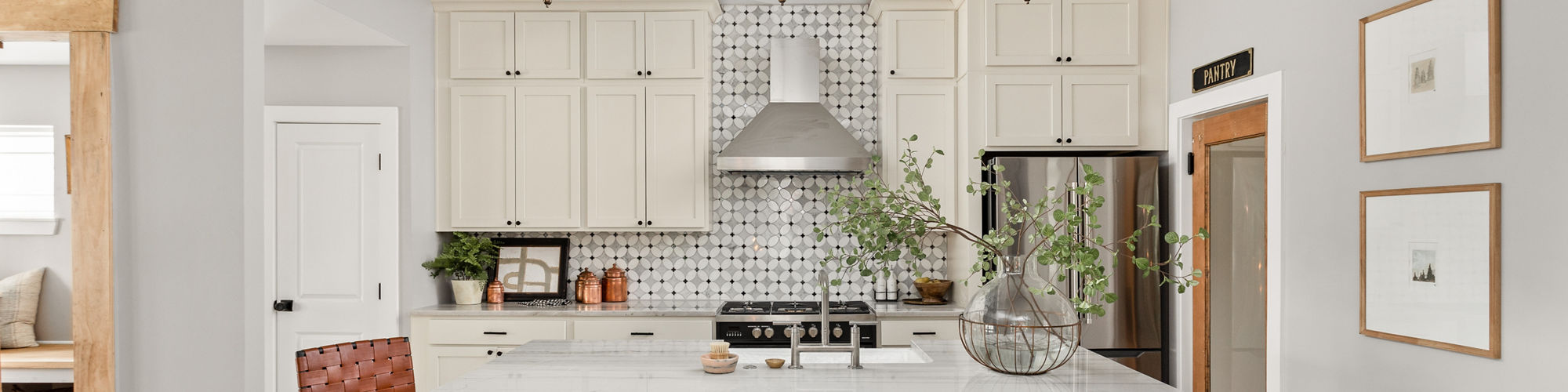 Kitchen with white and glass petal shaped mosaic backsplash, white quartz countertop, and white cabinets.