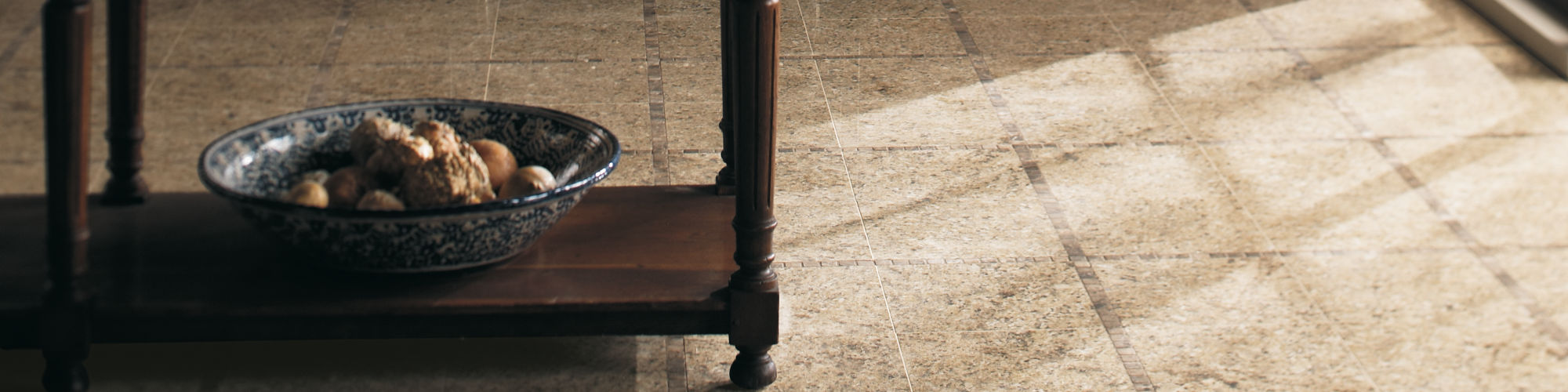 Kitchen with beige granite square tile on floor, wood cabinets, silver appliances, and dark wood table in the center.