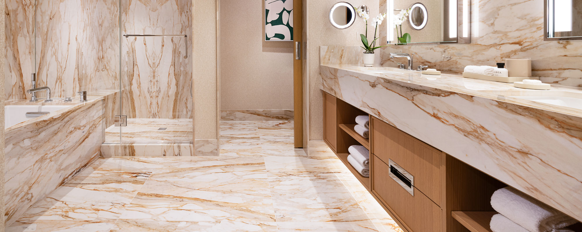 A contemporary bathroom features extensive white and beige marble on the floor, walls, bathtub, and shower area. A large double-sink vanity with wooden cabinetry and open shelving holds neatly folded towels and accessories. Vertical light fixtures fr