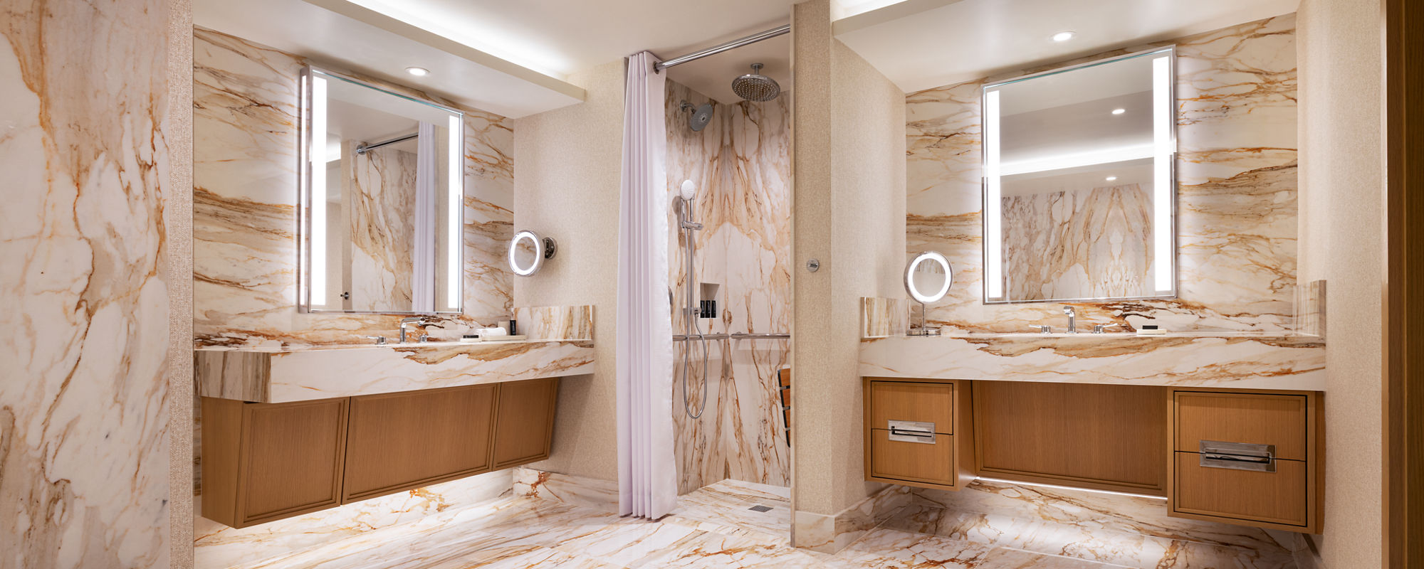 Spacious contemporary bathroom featuring extensive marble surfaces on the floor, walls, and countertops. The room includes two large vanities with underlit mirrors and wooden cabinetry on opposite sides. A central walk-in shower with a curtain and ra