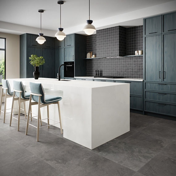 Kitchen with gray stone look square floor tile, blue cabinets, white monochromatic counter and island, blue chairs at island, and black weave mosaic on backsplash.
