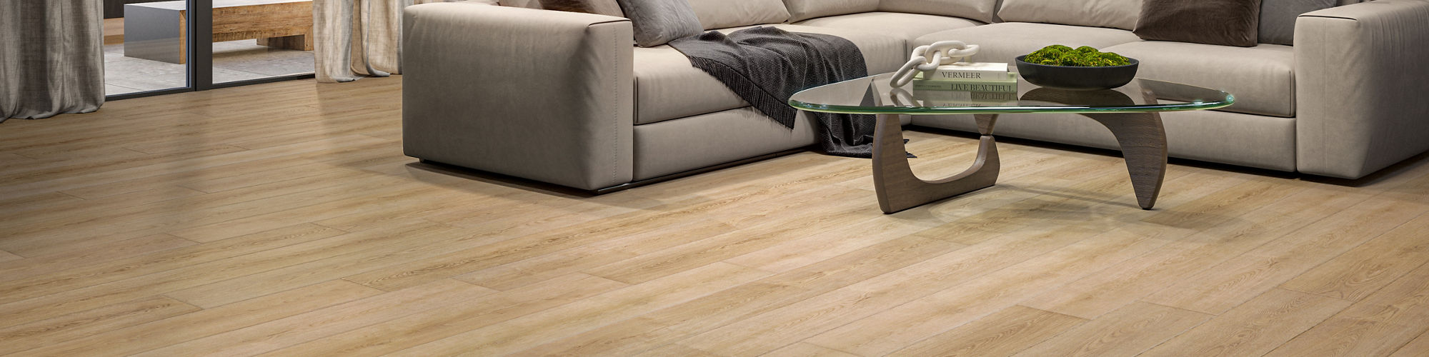 A large, contemporary living room features a light beige sectional sofa and a glass coffee table, set on wide plank wood flooring. 