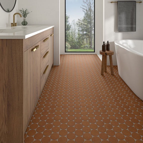 Bathroom with orange circle mosaic on floor, white tub, white walls, white countertop, wood cabinets, and large window showing the outdoors.
