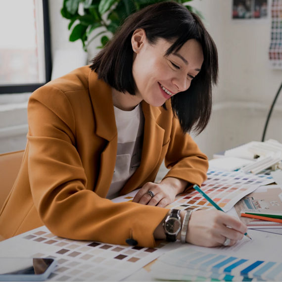 Interior designer smiling while reviewing color swatches and materials at a desk near a window.