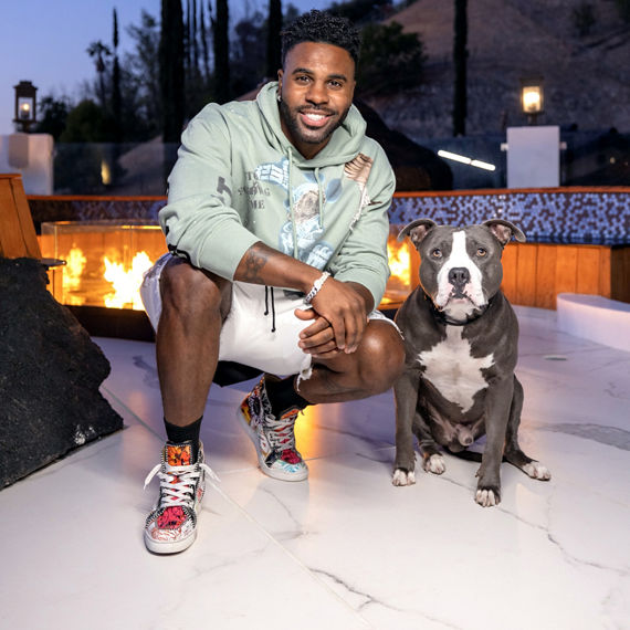 Jason Derulo and his canine companion, Ice, in front of his outdoor firepit with flooring made of white and gray vein porcelain slab that looks like marble.