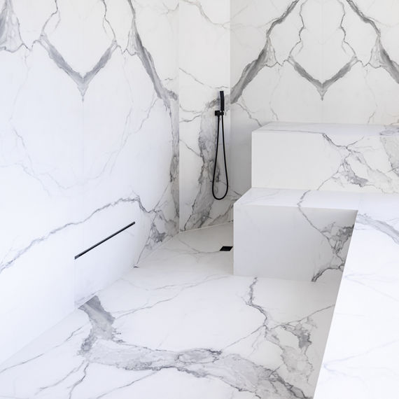 Steam room with black fixtures and white with gray veining porcelain slab that looks like marble on walls and floor.