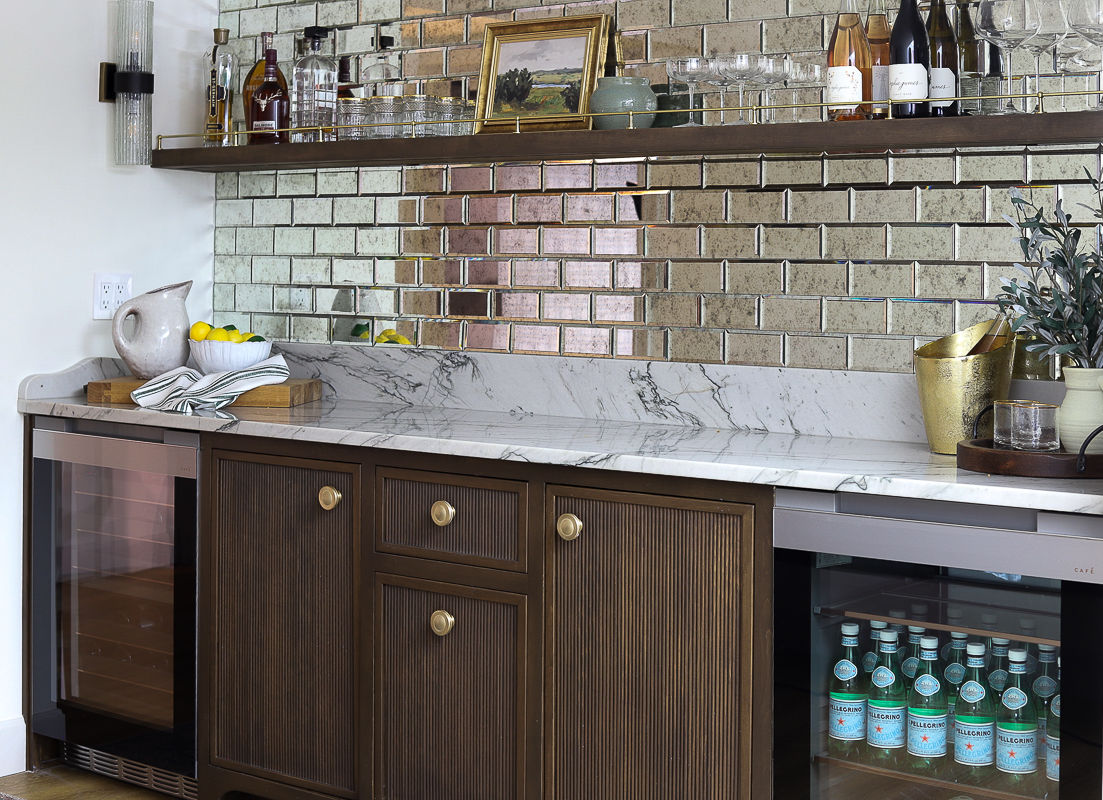 Basement bar with silver look subway tile on backsplash, white marble look quartzite slab on counter, and wood cabinets.