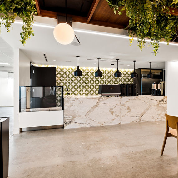 Lunch bar with white marble look porcelain slab counter on bar, beige floor, and wood and greenery as accents.