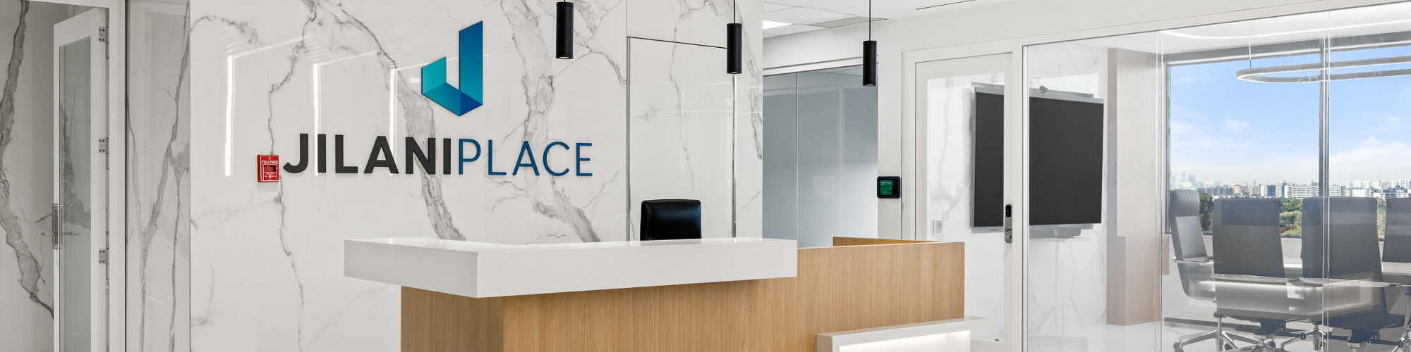 Welcome area with white marble look porcelain slab on floors and walls, light wood welcome desk, and office to right.