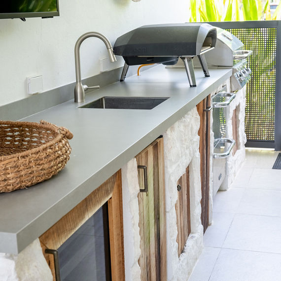 Outdoor kitchen with a gray porcelain concrete look slab on counter, white stone and wooden cabinets, and silver accents.