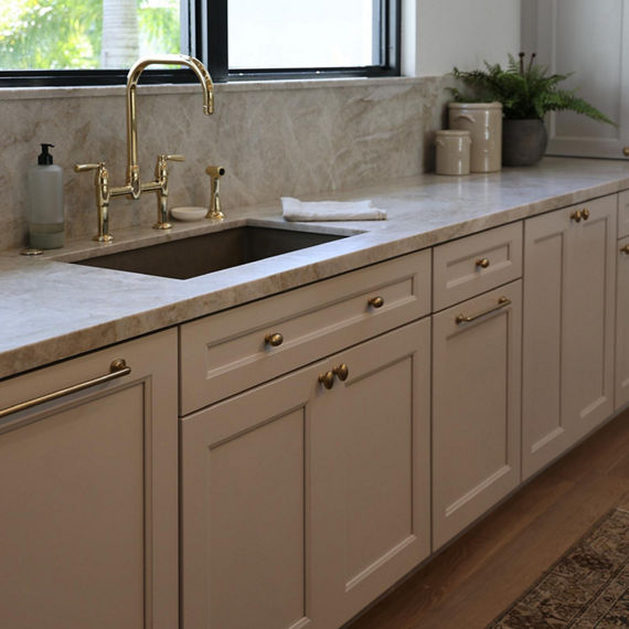 Kitchen with a beige quartzite slab on the backsplash and countertop, white cabinets, and wood floors.