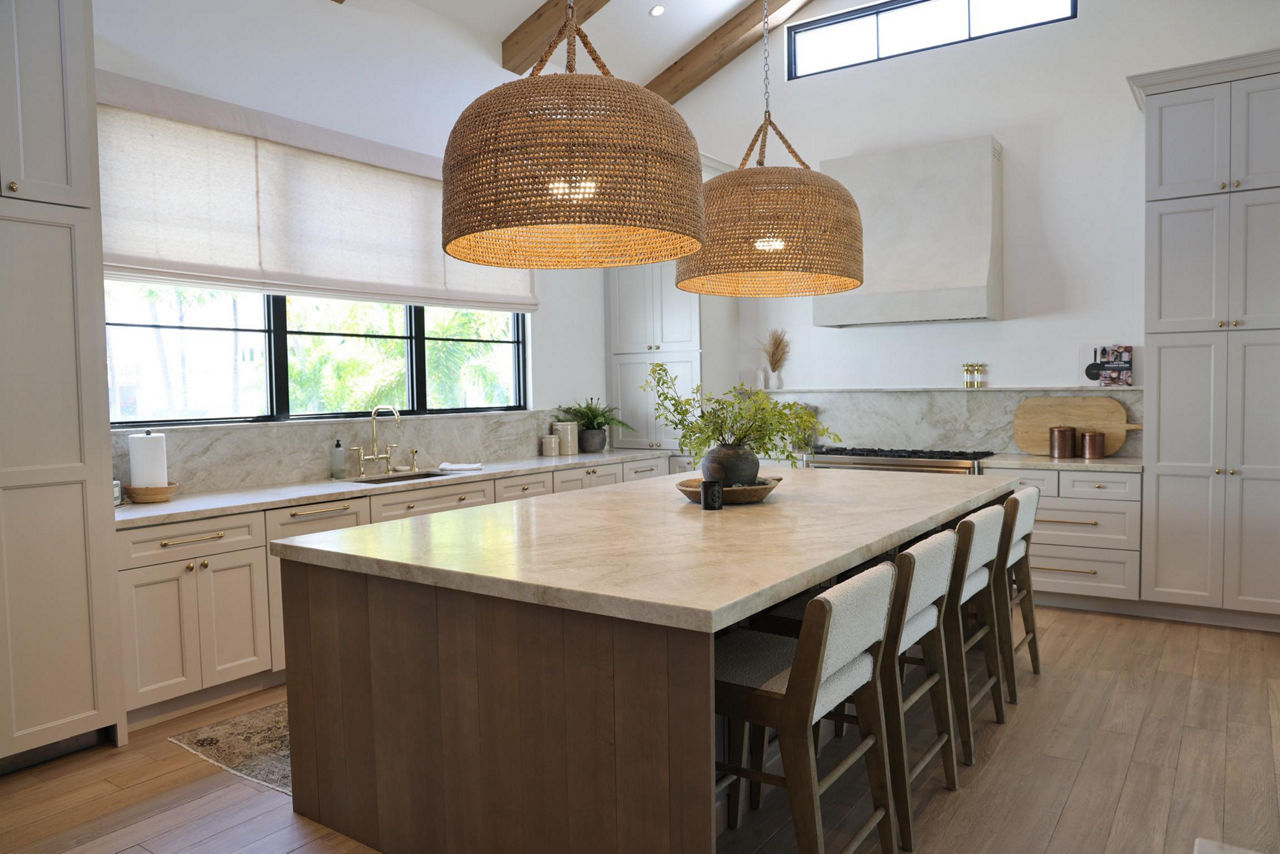 Kitchen with a beige quartzite slab on the backsplash and countertop, white cabinets, and wood floors.