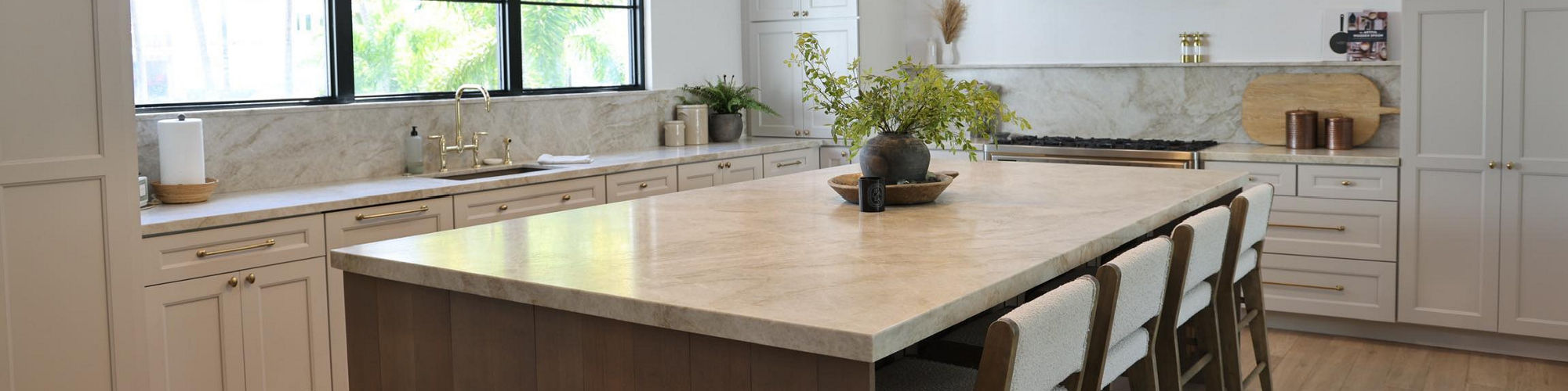 Kitchen with a beige quartzite slab on the backsplash and countertop, white cabinets, and wood floors.