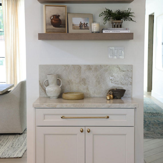 Kitchen with a beige quartzite slab on the backsplash and countertop, white cabinets, and wood floors.
