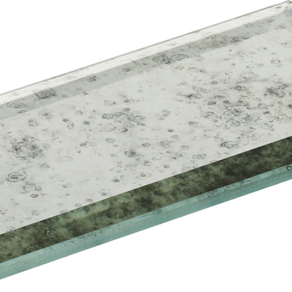 A single rectangular glass tile with a beveled edge is shown against a white background. The tile features an antique, distressed mirror finish with scattered speckled patterns across the surface. Its transparent edges reveal the thickness of the gla