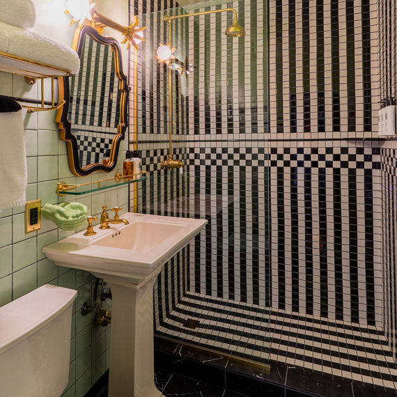 Hotel bathroom with black and white mosaic tile in shower in stripe pattern, white sink, green walls, and gold accents.
