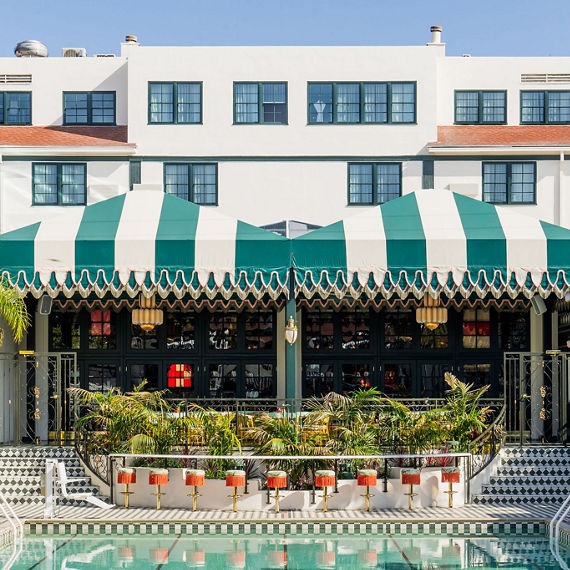 View of hotel pool and bar with off white and green mosaic tile, green and white sun shades, and orange bar stools.