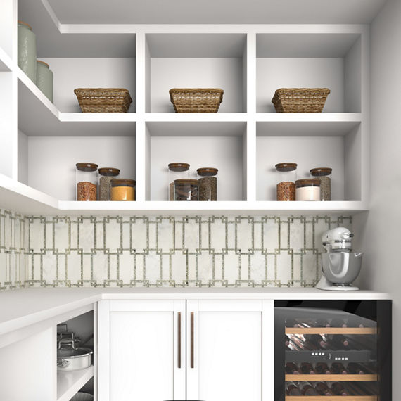 A contemporary pantry features white open shelving filled with woven baskets and glass jars of dry goods. Below the shelves, a patterned tile backsplash adds texture above sleek white cabinets. A countertop stand mixer sits in the corner next to a bu