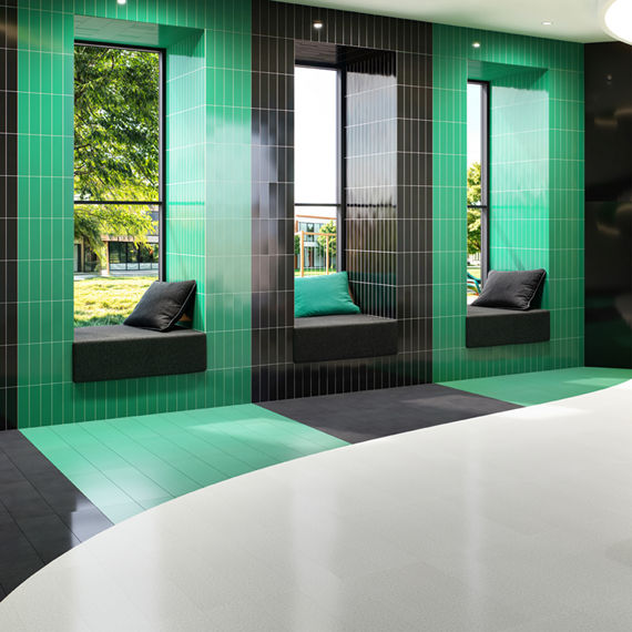 Library with green and black rectangle fabric look tile on walls and accenting floor, white rectangle floor tile, and books on a shelf.