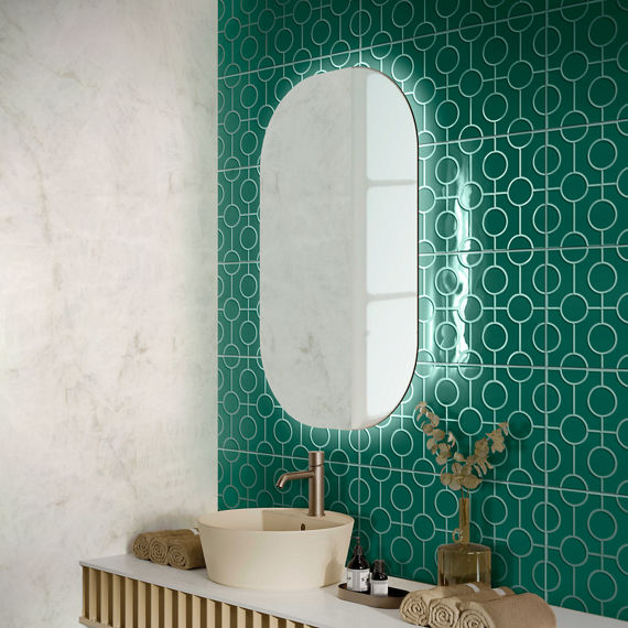 Bathroom sink with white countertop, gold counter, gold hand towels and accents, capsule shaped mirror, and a teal encaustic wall tile on backsplash.