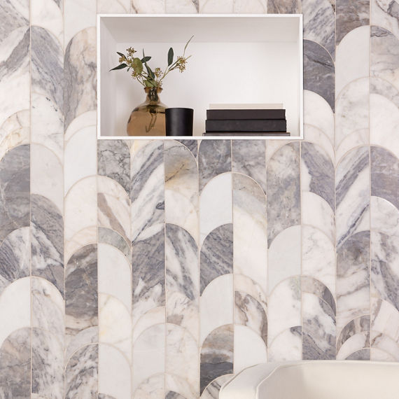 Seating area with marble look arch mosaic on wall, white wall niche with books and plant, and white chair.